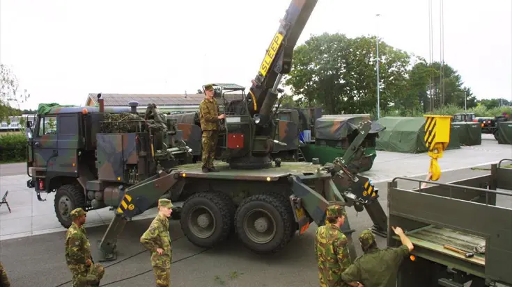 DAF YBZ-3300 takelauto staat op het punt  een voertuig op te tillen met uitgeschoven kraan. Meerdere militairen kijken toe.