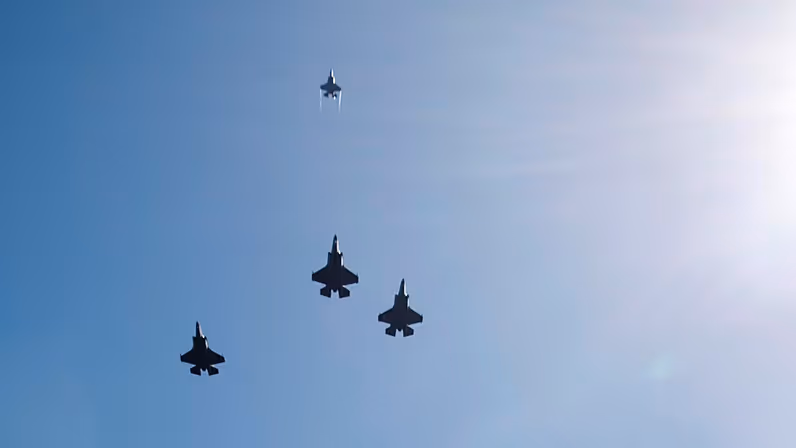 ‘Drie F-35’s vliegen naast elkaar, een vierde exemplaar vliegt recht omhoog. Rechts is de zon te zien.