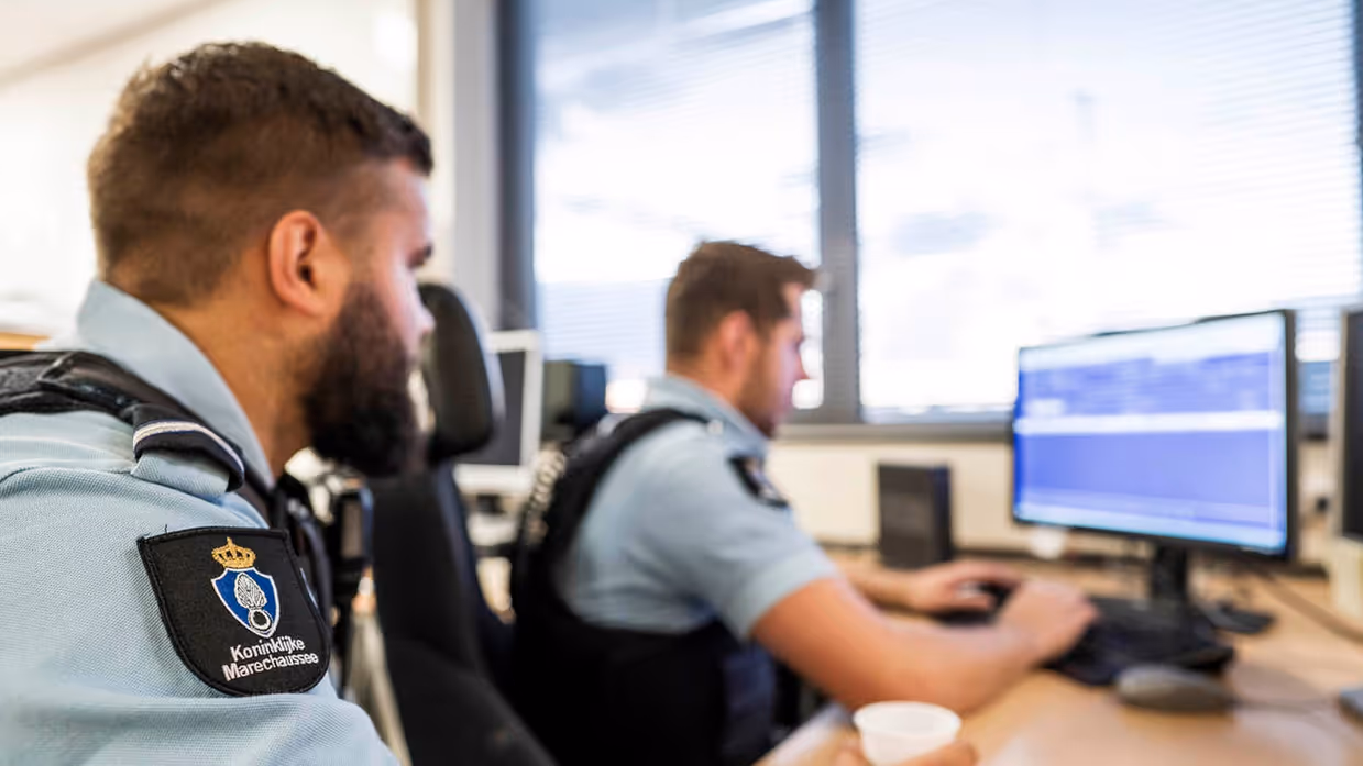 Twee marechaussees kijken naar het PC-scherm.