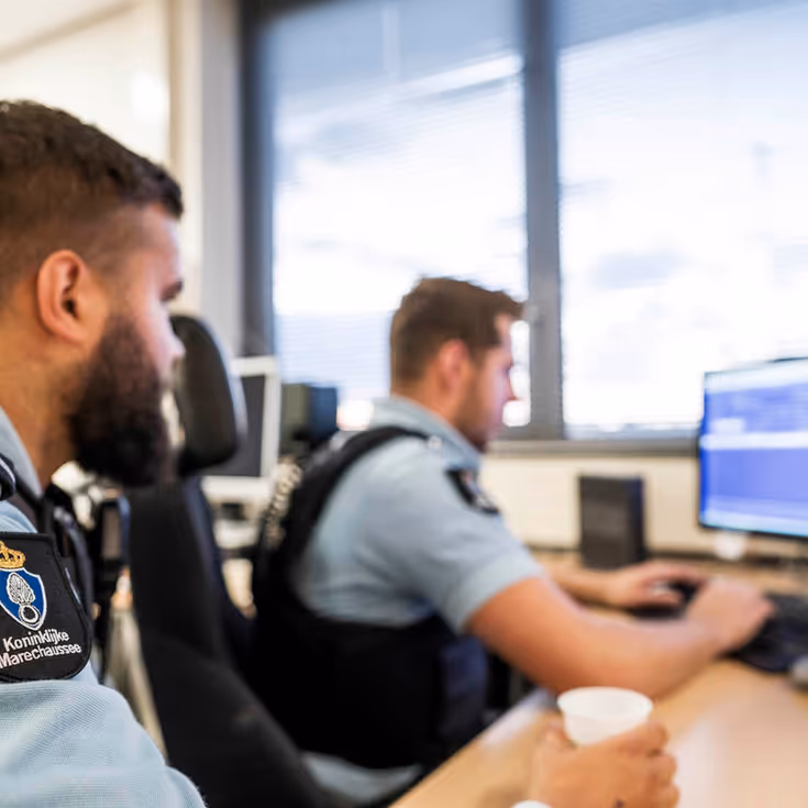 Twee marechaussees kijken naar het PC-scherm.