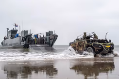 LCU-landingsvaartuig ligt vlakbij het strand, en een Fennek-verkenningsvoertuig met 2 militairen erin rijdt op de voorgrond. 
