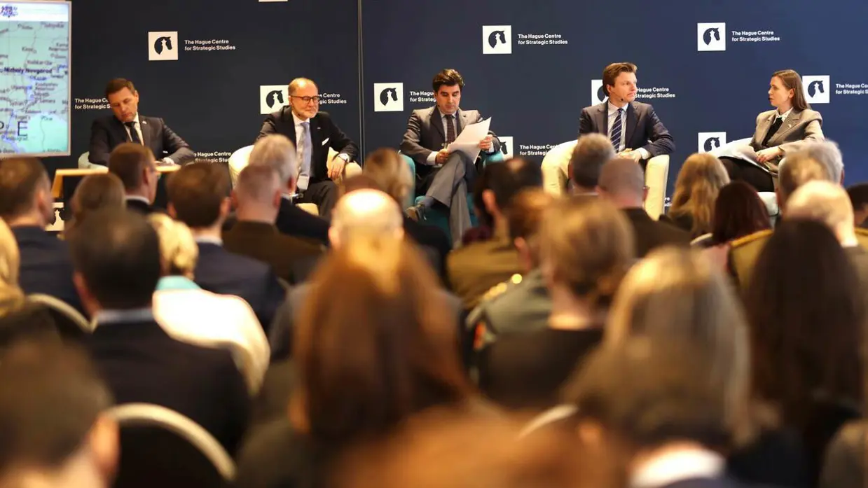 Vier ministers van Defensie zitten naast elkaar tijdens een panel. Op de voorgrond de hoofden van de aanwezigen.