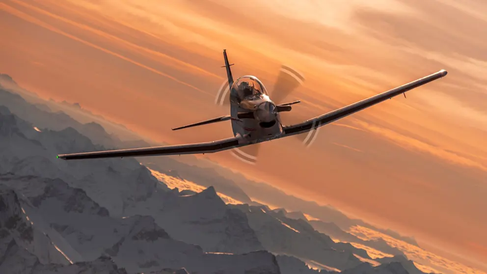 Een PC-7 MKX vliegt in de lucht in een bergachtige omgeving.