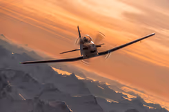 Een PC-7 MKX vliegt in de lucht in een bergachtige omgeving.