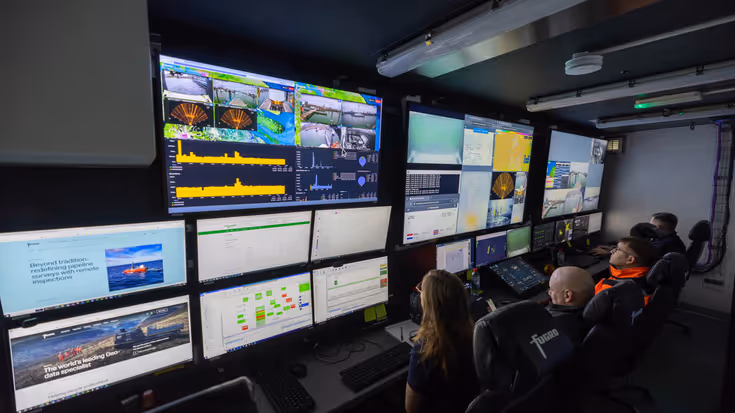 Mensen zitten in ruimte vol met schermen. 