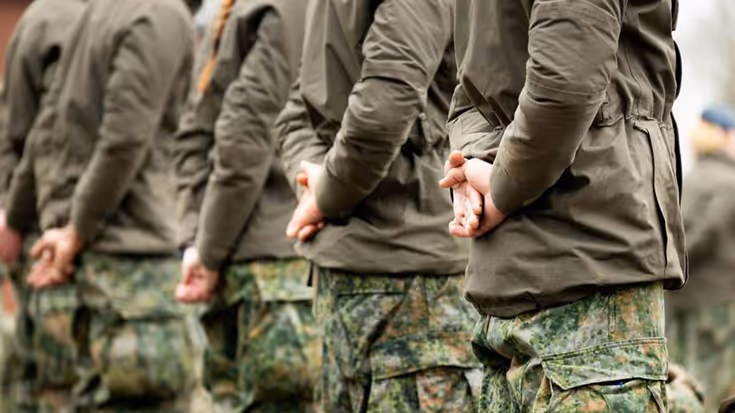 Vijf militairen zij aan zij schuin van achteren gefotografeerd.