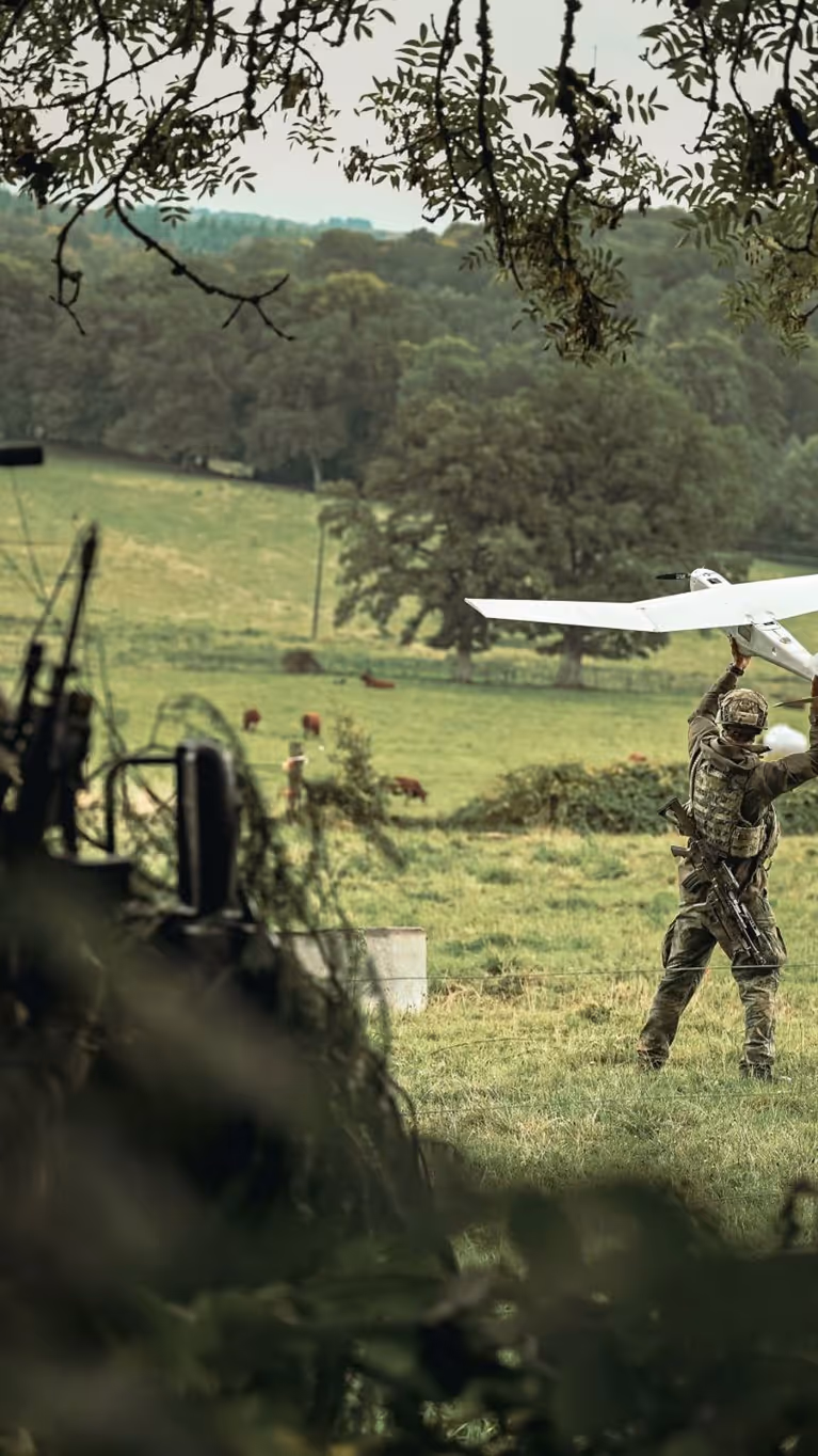 Een militair werpt een drone vooruit in een grasveld.