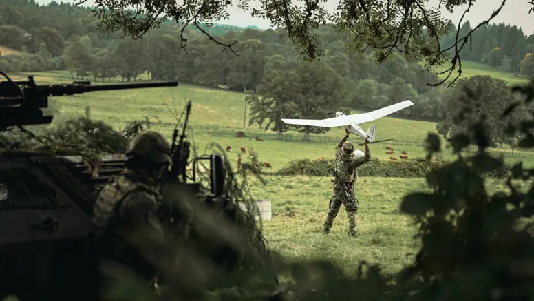 Een militair werpt een drone vooruit in een grasveld.