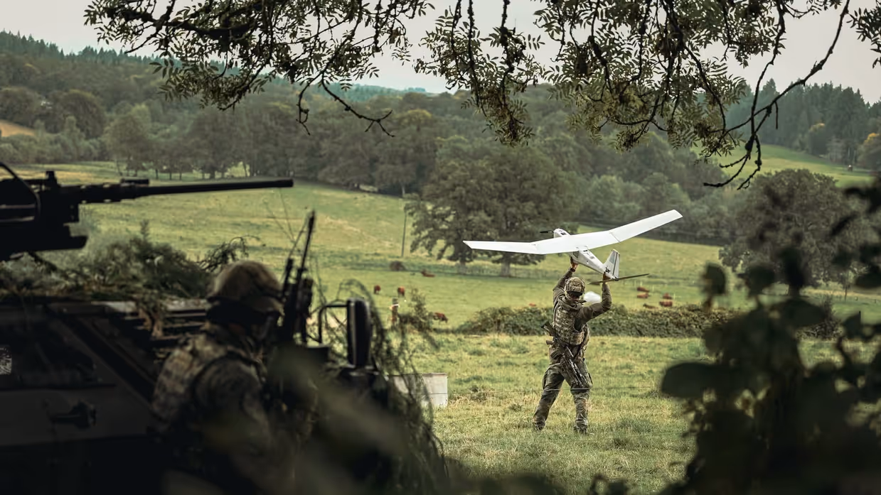 Militairen en een drone in en net naast een bosrand.