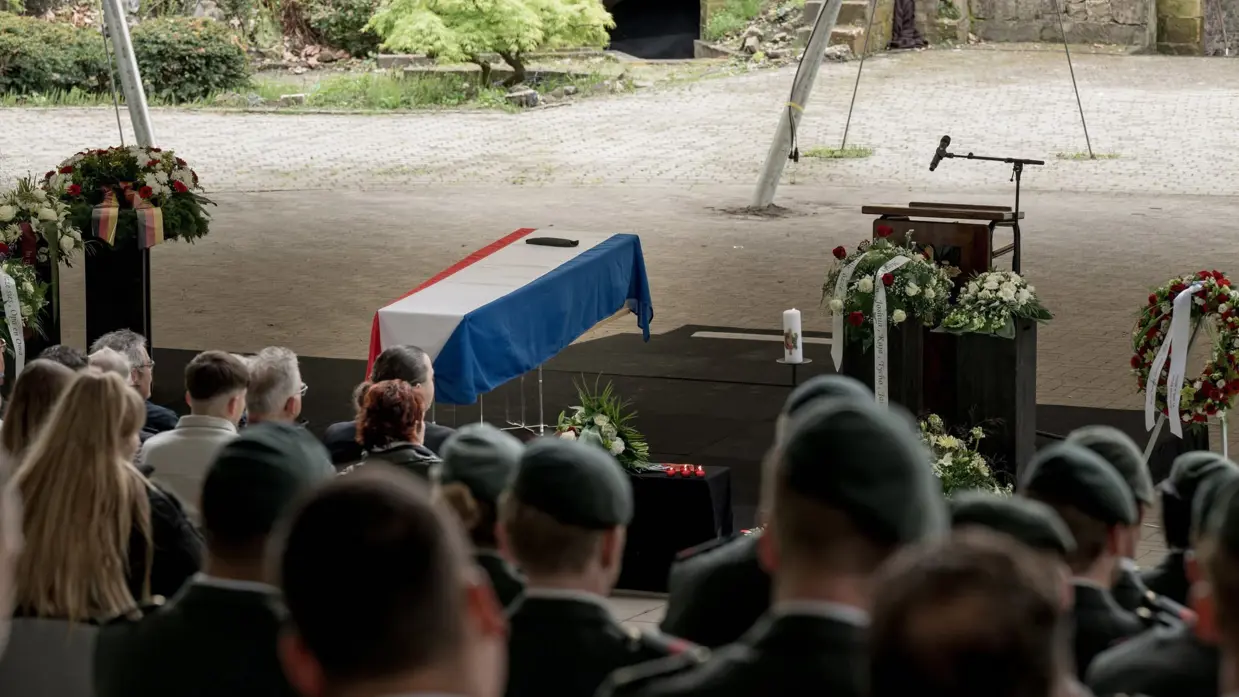 Mix van beelden van Delano. We zien onder meer zijn kist gedragen door militairen, een groepsappel met trompet en een herdenkingsplek voor de gevallen militair.&nbsp;