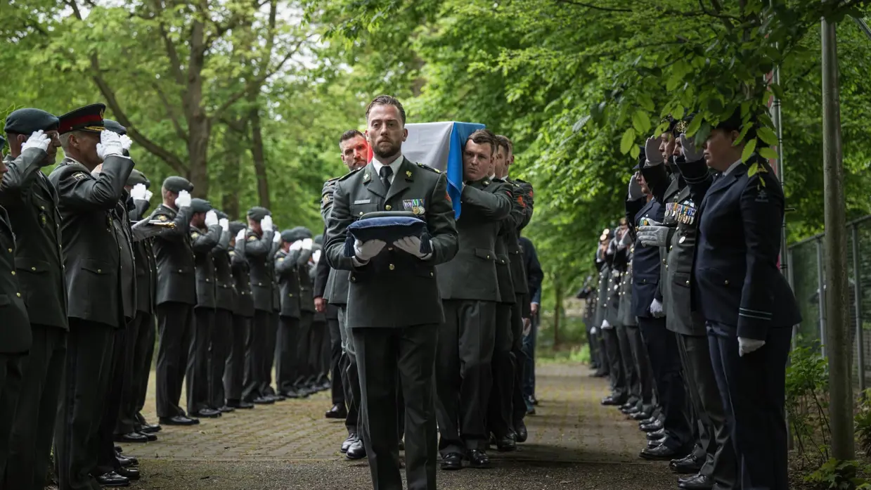 Mix van beelden van Delano. We zien onder meer zijn kist gedragen door militairen, een groepsappel met trompet en een herdenkingsplek voor de gevallen militair.&nbsp;