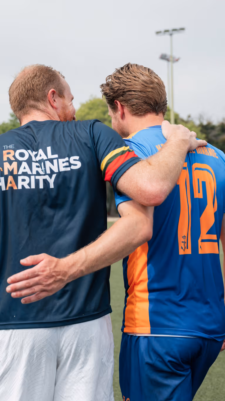 Nederlandse en Engelse mariniers lopen gearmd op het voetbalveld.