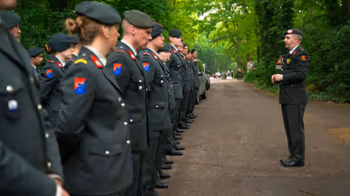 Luitenant Kleinbloesem spreekt reservisten toe Twee reservisten lopen met een krans 