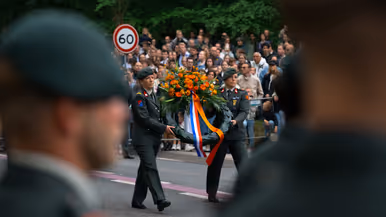 Luitenant Kleinbloesem spreekt reservisten toe Twee reservisten lopen met een krans 