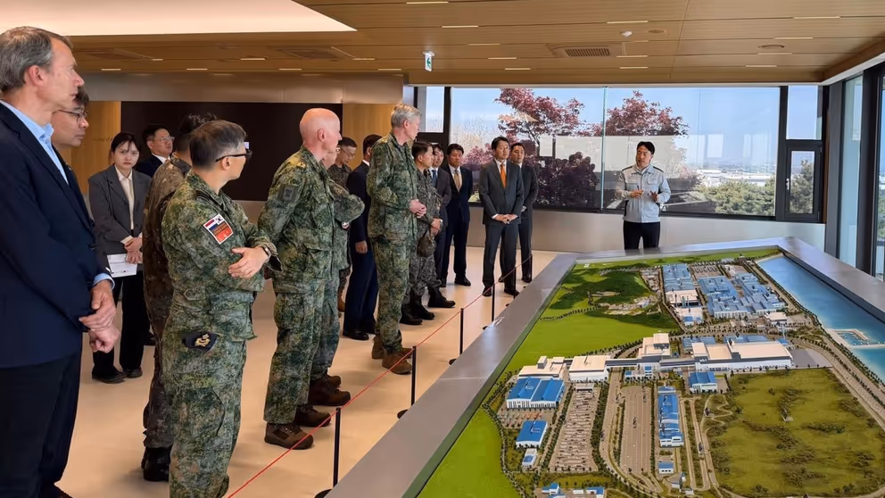 Militairen en burgers kijken naar een groene maquette.