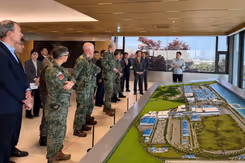 Militairen en burgers kijken naar een groene maquette.