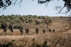 Militairen met bepakking lopen in een rij door natuurgebied.