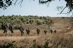 Militairen met bepakking lopen in een rij door natuurgebied.