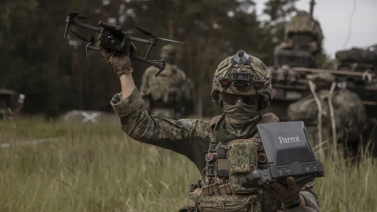 Een militair in het groen staat op het punt een drone te lanceren vanuit zijn hand.