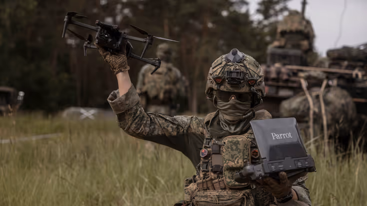 Een militair houdt een drone in de lucht. 