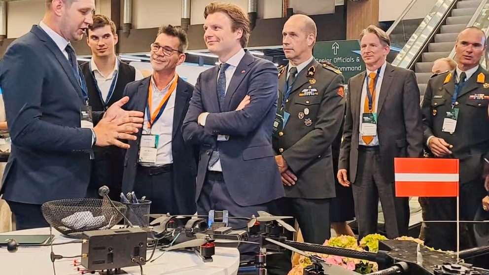 Brekelmans en anderen luisteren bij tafel met drone naar uitleg.