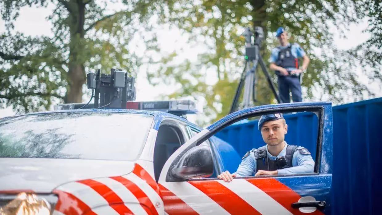 Twee marechaussees poseren bij hun auto en op een container vanaf waar ze drones besturen.