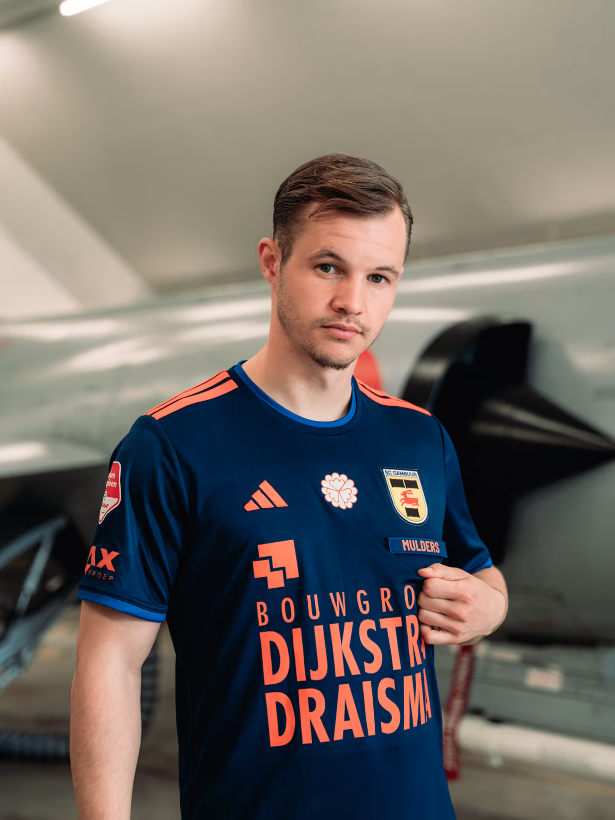 vier mannen in formele kleding op een voetbalveld tijdens een Veteranen-wedstrijd. Een symbool met "Opdat wij niet vergeten" staat centraal.