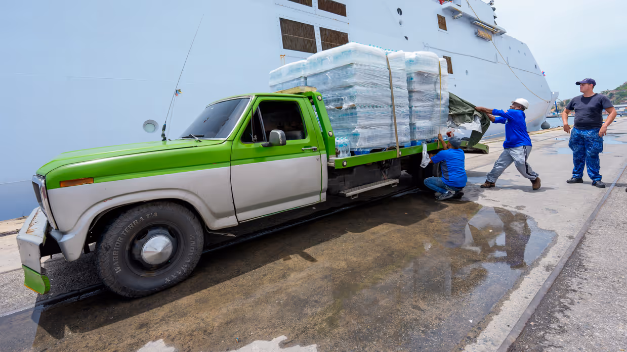 Een oude pick-up truck wordt volgeladen met pallets waterflessen. 