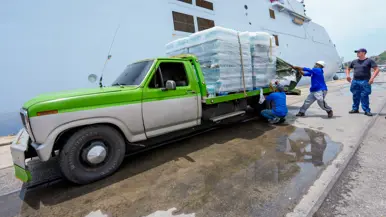 Een oude pick-up truck wordt volgeladen met pallets waterflessen. 