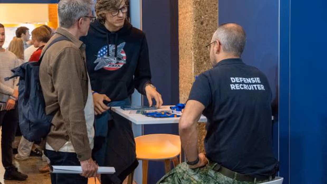 2 bezoekers staan bij een stand met informatie van een recruiter.