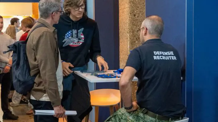 2 bezoekers staan bij een stand met informatie van een recruiter. 