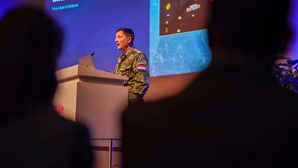 Een man in groen pak achter spreekgestoelte