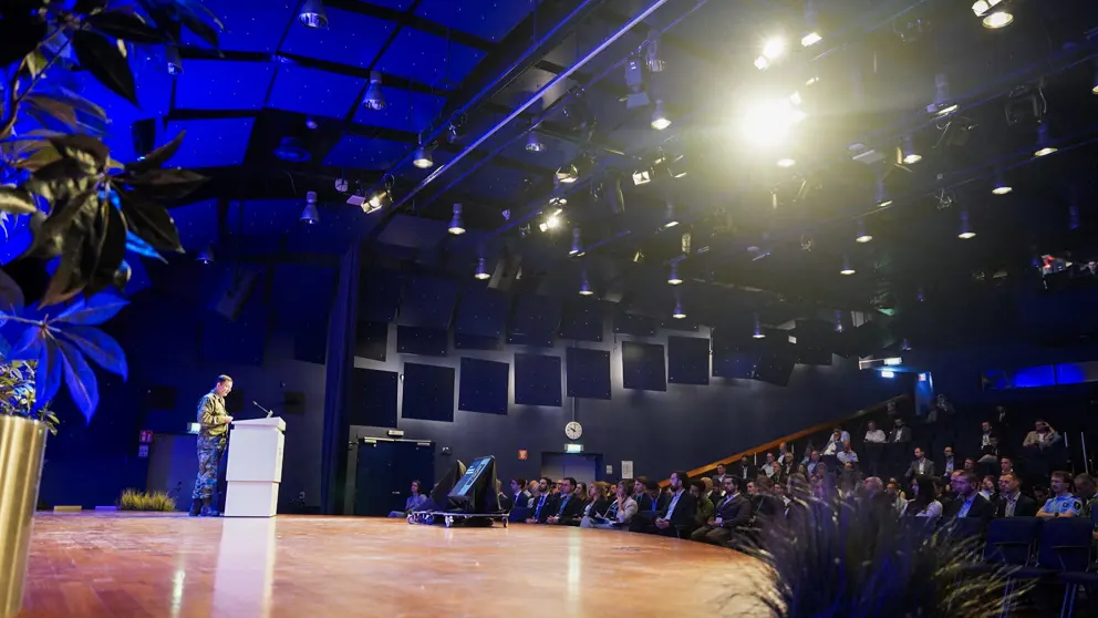 Een man voor een spreekgestoelte voor een gevulde zaal