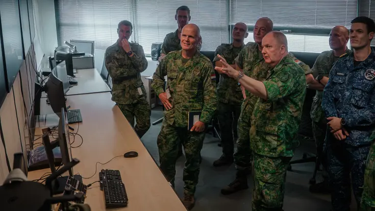 Militairen staan in een ruimte naar schermen te kijken.