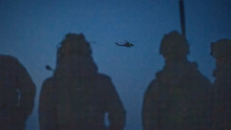 Twee FST-leden met een helikopter in de lucht op de achtergrond. 