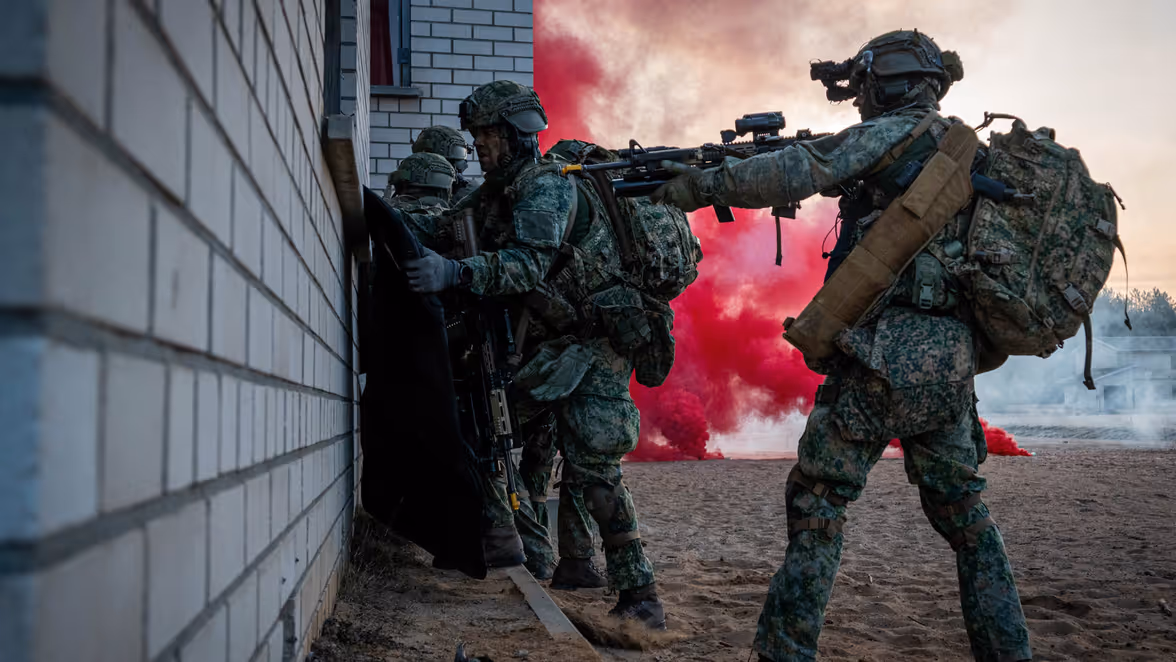 Militairen naast rode rook naast een gebouwtje.