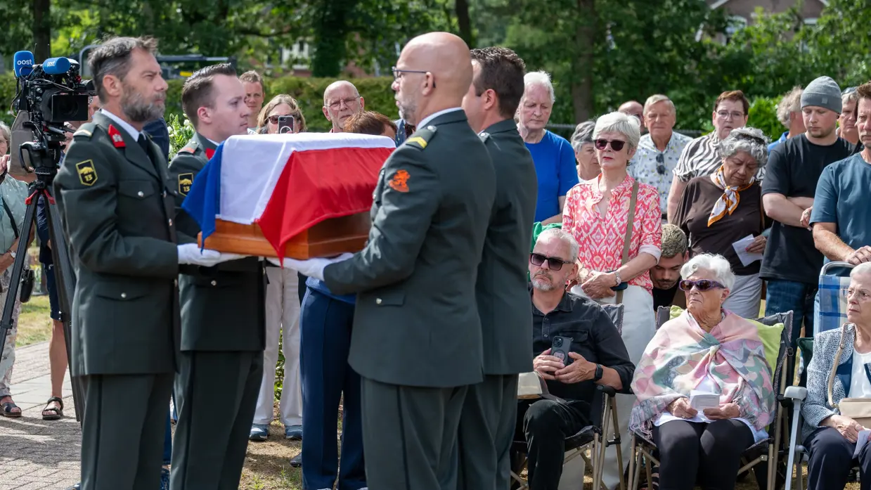 Militairen houden de kist vast met op de achtergrond de familie.