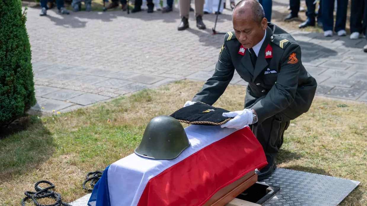 Een militair legt een foto en een medaille op de kist.