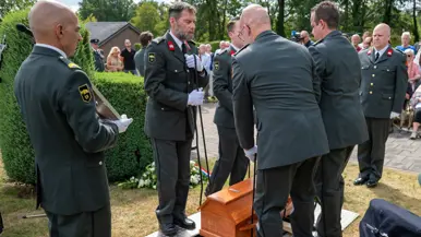 Met de touwen in de hand laten de reservisten de kist in het graf zakken.