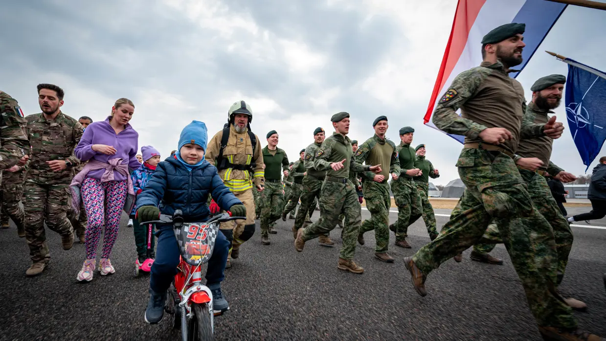 Militairen en burgers rennen over een landingsbaan. 