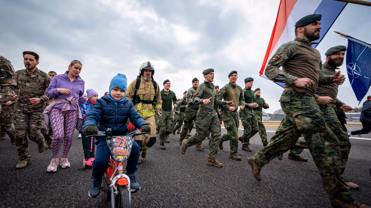Militairen en burgers rennen over een landingsbaan. 