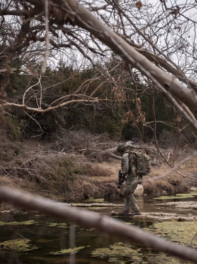 Militair steekt via lage rotsen een rivier over.