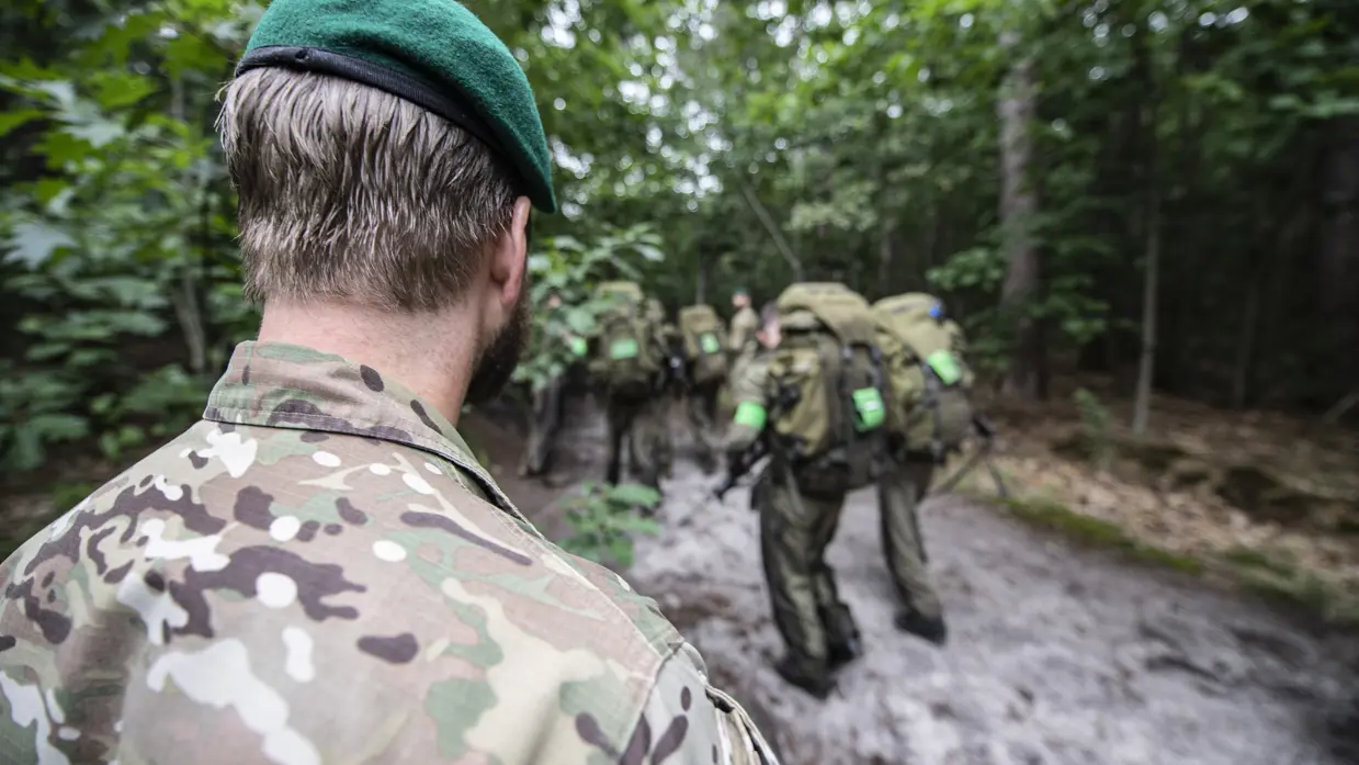 Een instructeur met groene baret kijkt hoe cursisten zich tijdens de commando-opleiding in groene overals verplaatsen.