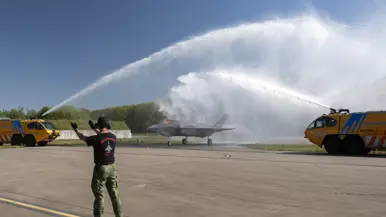 Twee gele brandweerauto’s spuiten van weerszijden een waterboog over de F-35 met staartnummer F-052.