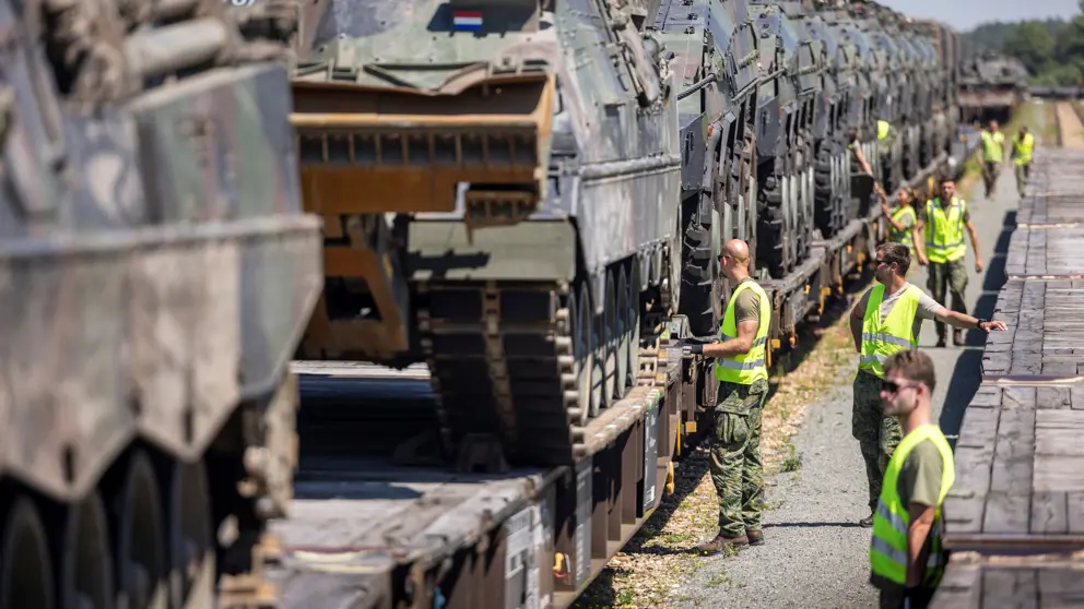 Militairen inspecteren tank die op een wagon staan.