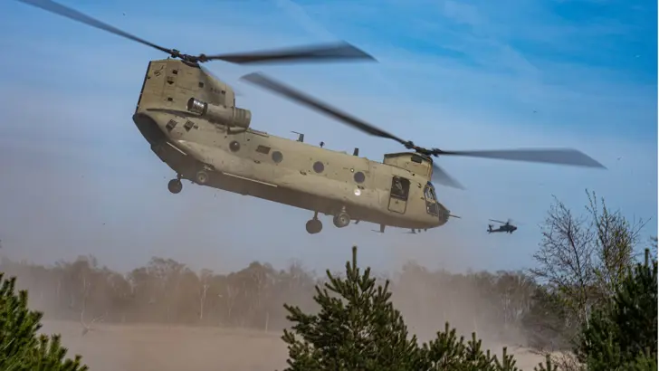 Een Chinook-transporthelikopter stuift zand op bij het opstijgen.