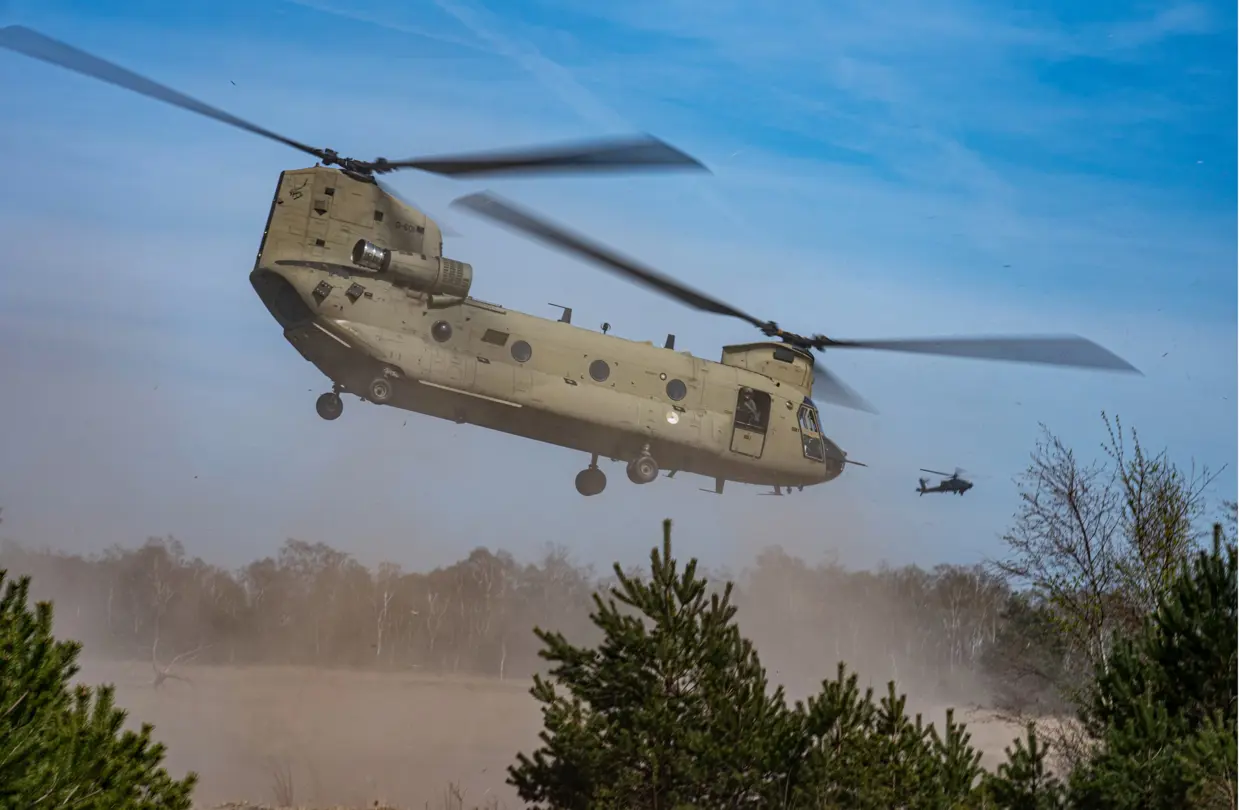 Een Chinook-transporthelikopter stuift zand op bij het opstijgen.