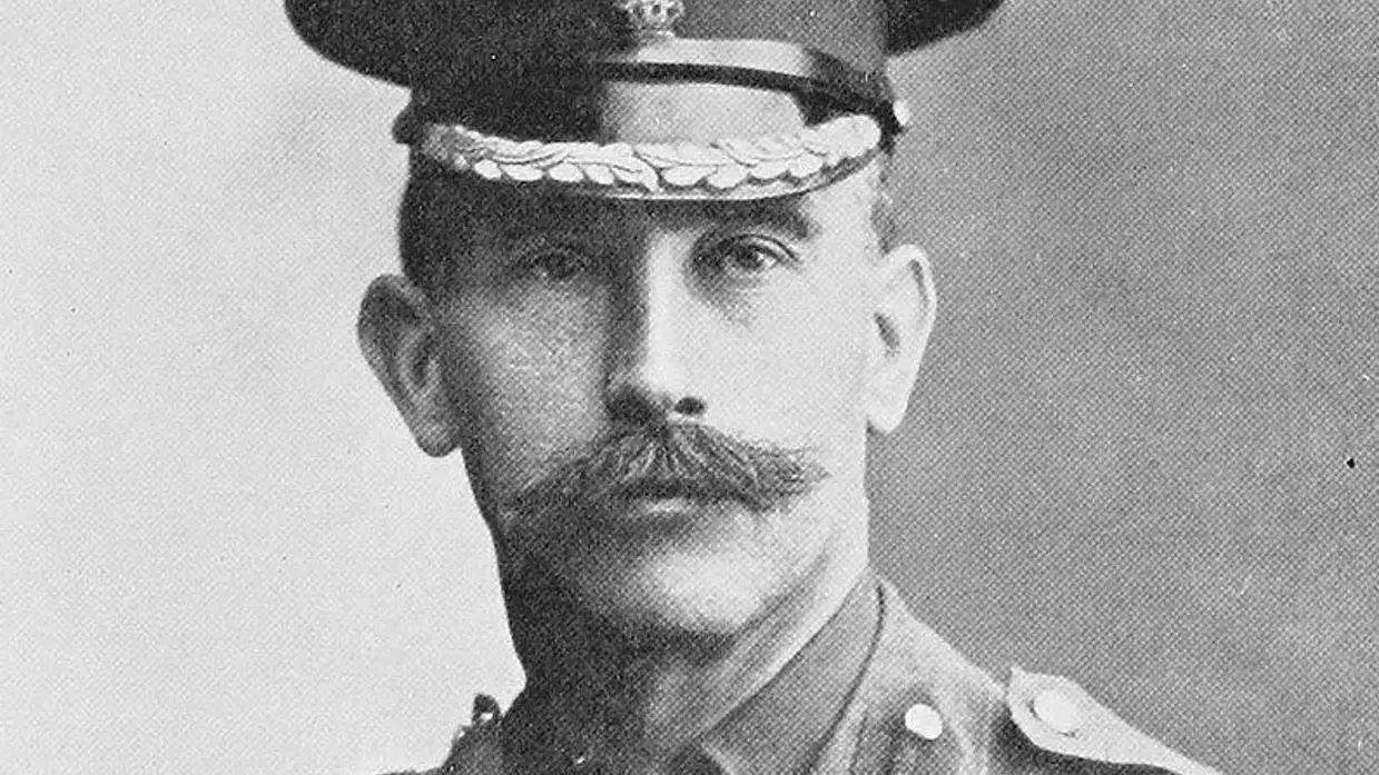 Een zwart-witportret van een man met een snor, in militair uniform met een pet en decoraties. 