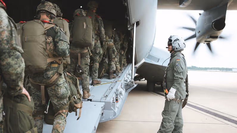 Militairen met parachute-uitrusting lopen via de laadklep een Duits A400M-transportvliegtuig binnen, terwijl een bemanningslid toezicht houdt naast het toestel.&nbsp;