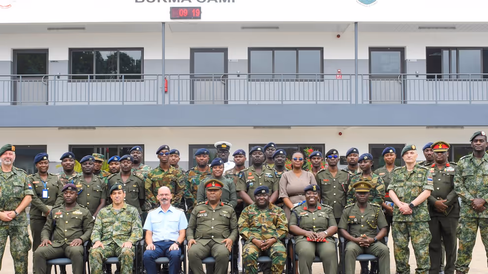 Groepsfoto van Nederlandse trainers en lokale militairen voor een trainingslocatie. 
